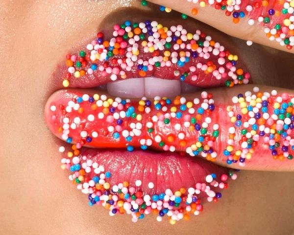 Close-up of lips and finger covered in colorful sprinkles.