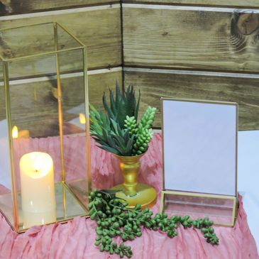 Centerpiece with glass square lanterns, greenery, and table runner.