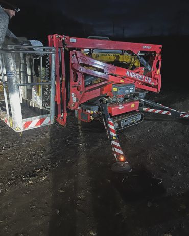 Red lift machine at night on dirt ground.