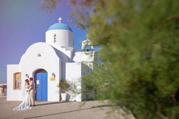 Couple kissing in front of a white church with blue dome.