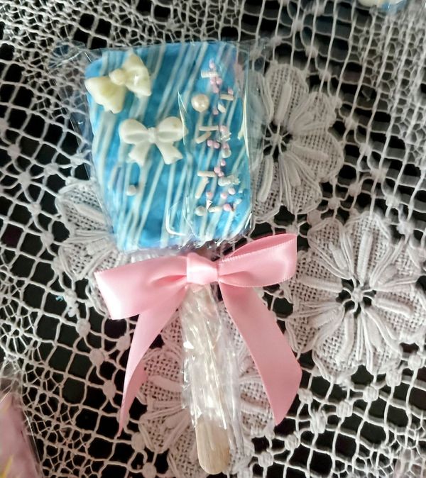 Blue decorated treat on a stick with a pink bow, placed on a lace tablecloth.