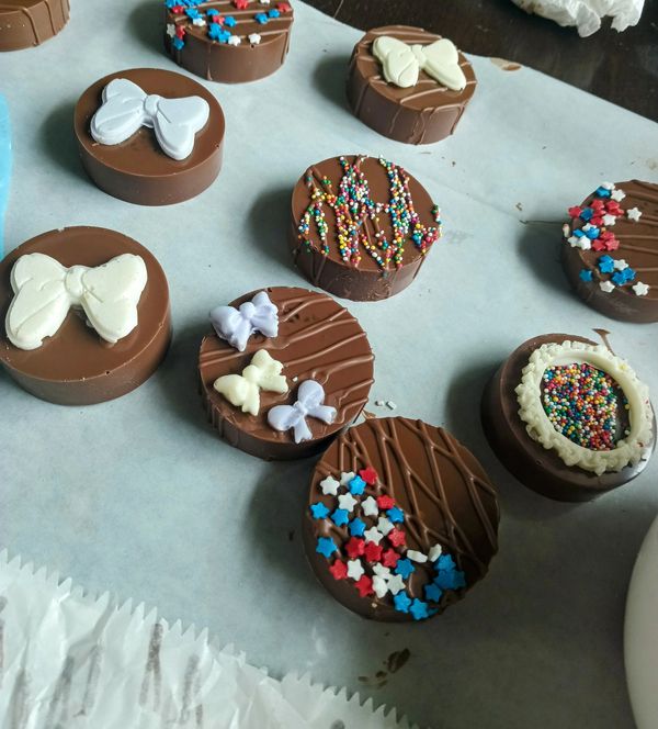 Decorated round chocolate pieces with colorful sprinkles and white chocolate bows.