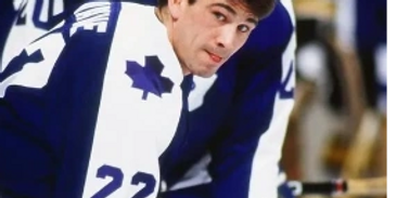 Ice hockey player in a blue and white uniform leaning forward on the ice.