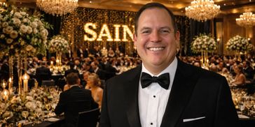 A smiling man in a tuxedo at a formal event with elegant decor.