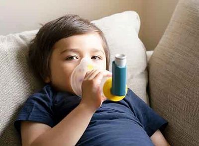Asthmatic child taking MDI with spacer with mask by himself happily