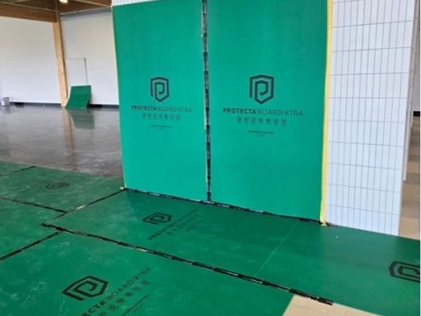 Green protective floor and wall panels with logo in an indoor space.