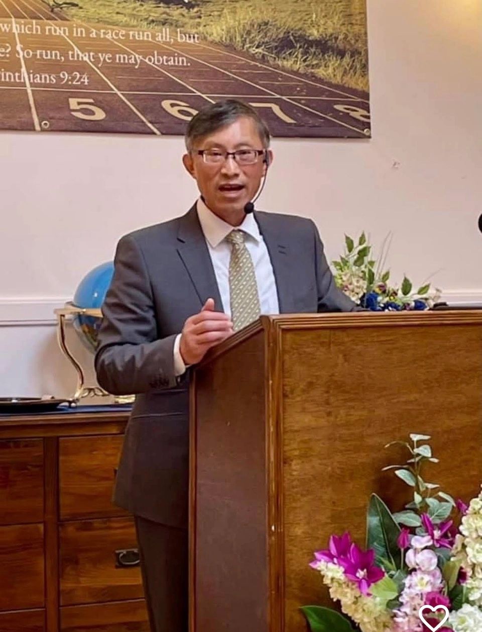 Man in suit speaking at a podium with flowers.