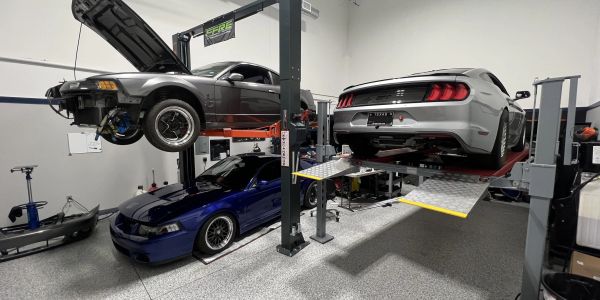 Three muscle cars in a garage, two on lifts.