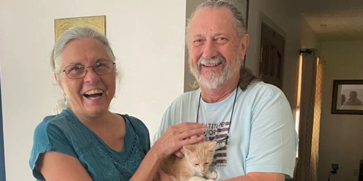 Woman and man with gray hair holding an orange kitten. The woman is laughing and the man is smiling.