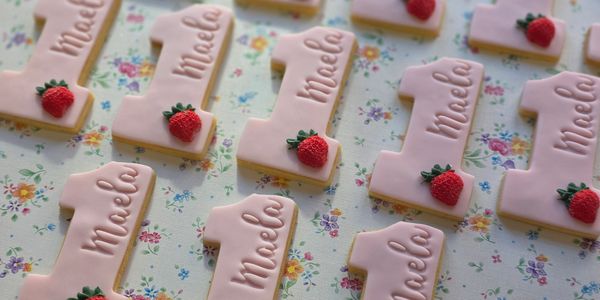 Pink number one cookies with strawberries and the name Miela.