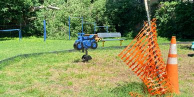 Orange safety fence and traffic cone near a blue playground ride-on toy.