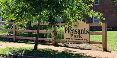 Sign for Pleasants Park at 401 S. Laurel St. near a tree and wooden fence.