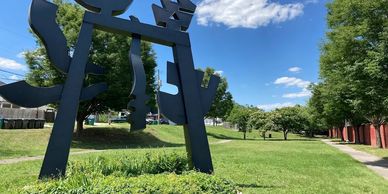 Large black sculpture in a green park under blue sky.