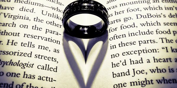 Black ring on an open book casting a heart-shaped shadow—symbolizing love.