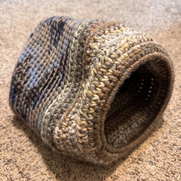 Handmade crochet basket with earthy tones on a carpeted floor.