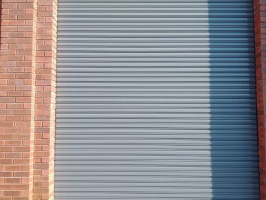 A closed gray rolling shutter door next to a red brick wall.