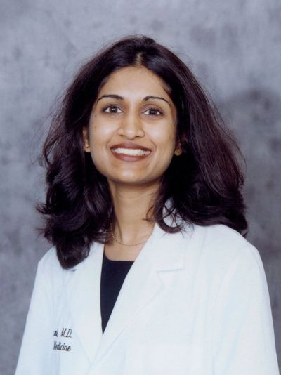 Smiling female doctor in white coat against gray background.