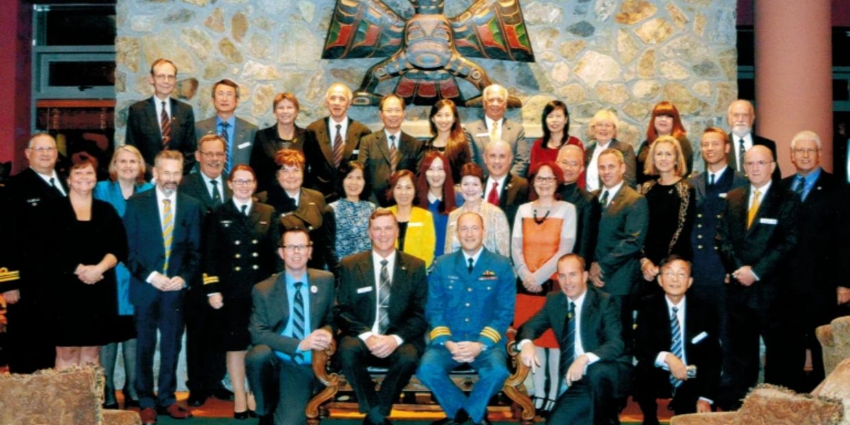 Large formal group photo in front of a stone wall with a carved totem.