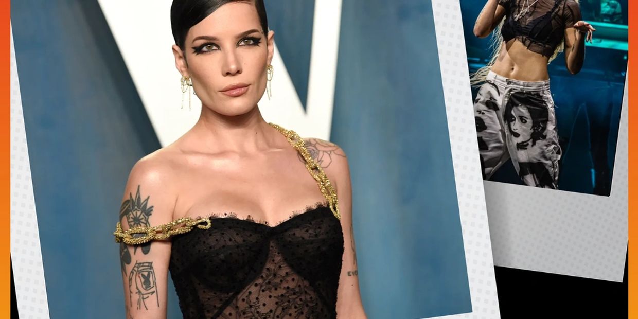Woman in a sheer black dress with gold chain detail and tattoos poses confidently.