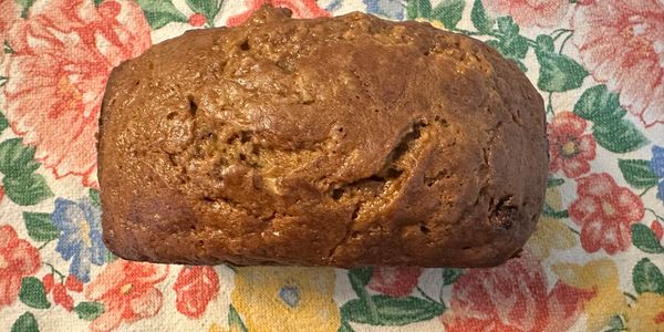 Freshly baked brown loaf of bread on a floral tablecloth.