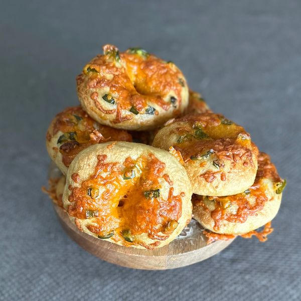 Cheesy bagels topped with herbs on a wooden platter.