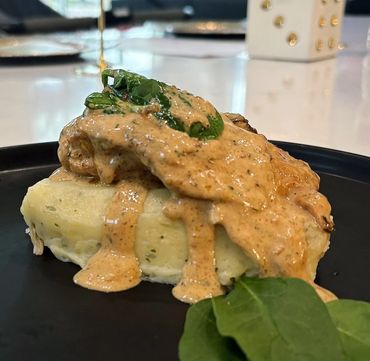 Mashed potatoes topped with creamy sauce and spinach on a black plate.