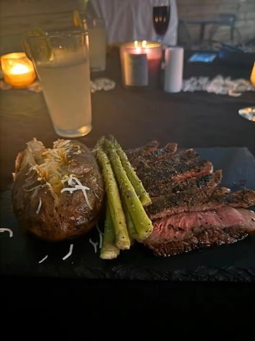 Steak dinner with baked potato, asparagus, and drinks.