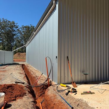 Construction site with trench and tools beside a metal building under a clear sky.