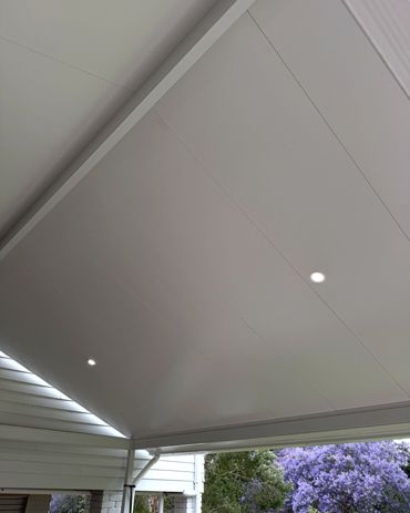 Modern white ceiling with recessed lights and purple flowering trees outside.