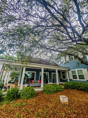 A charming blue house with a porch under a large tree.