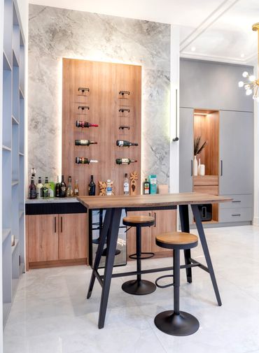 Modern home bar with wood and marble accents, featuring a tall table and stools.