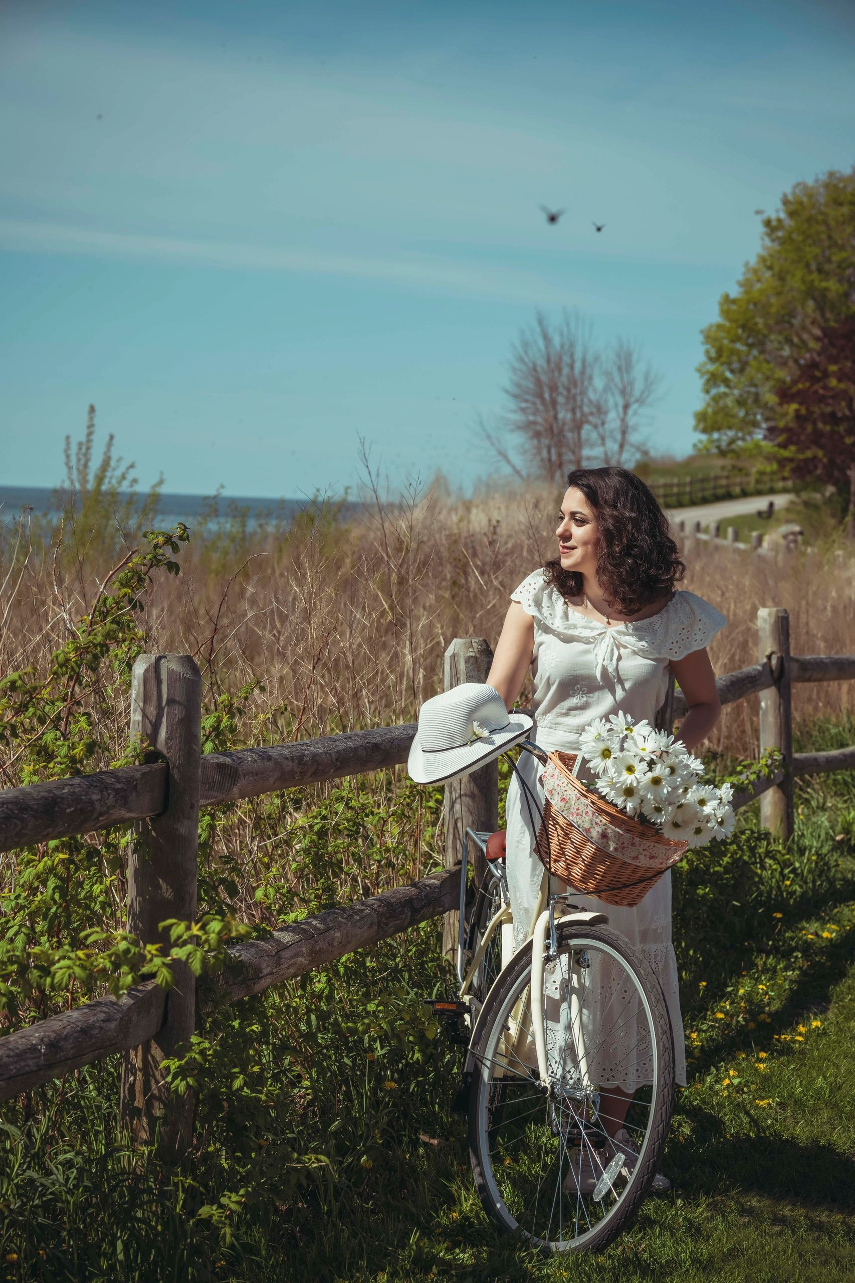 Woman with a bicycle and flowers enjoys a sunny day by a wooden fence. Emotional outdoor portrait wi