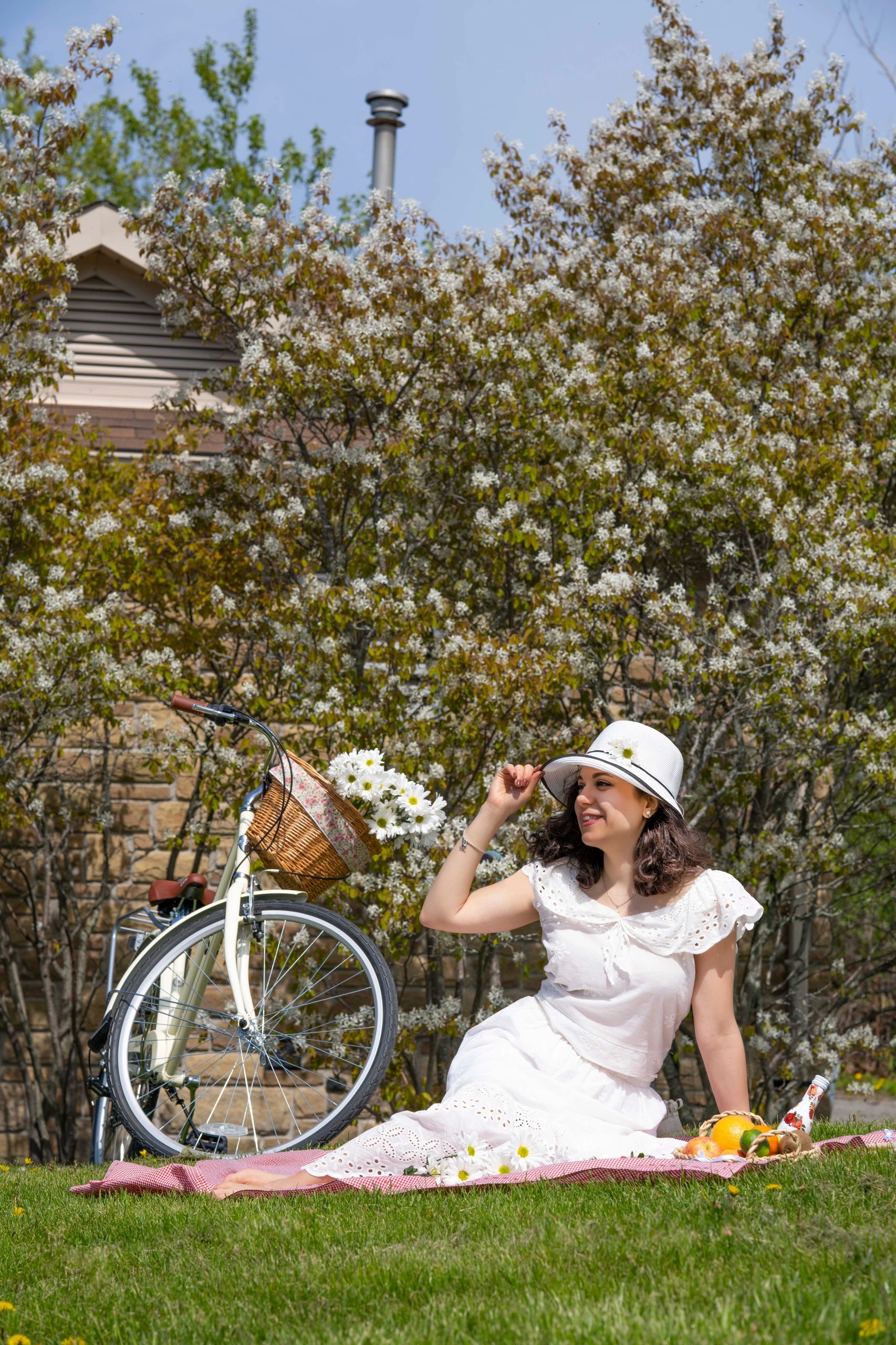 A woman in white enjoys a sunny picnic with a bicycle and flowers nearby.