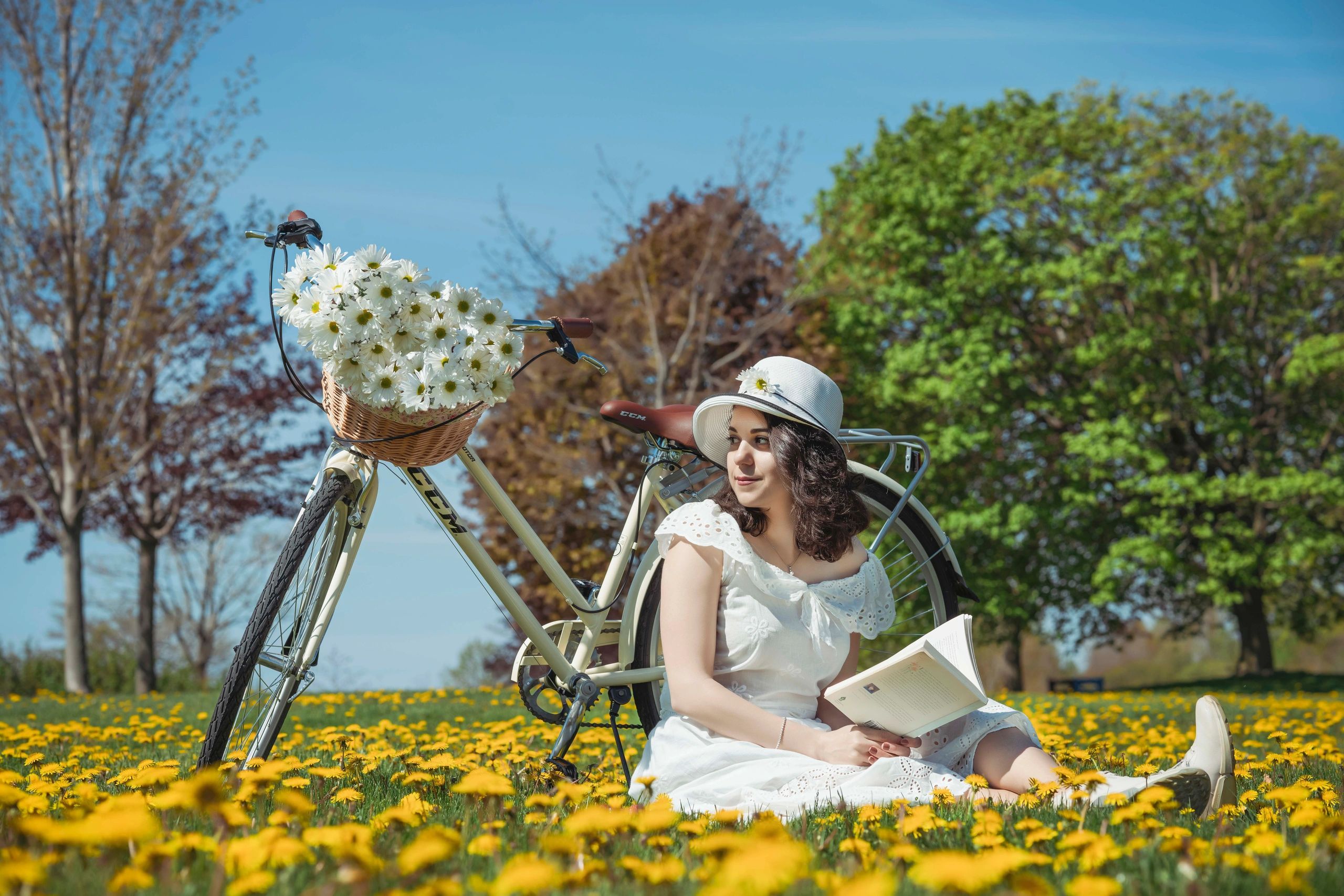 Woman in white dress reading by a flower-filled bicycle in a sunny field. Cinematic emotional portra