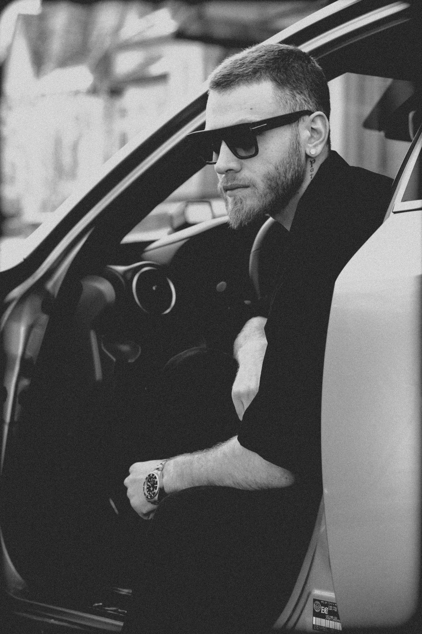 A man with sunglasses sitting in a car door, looking outside.