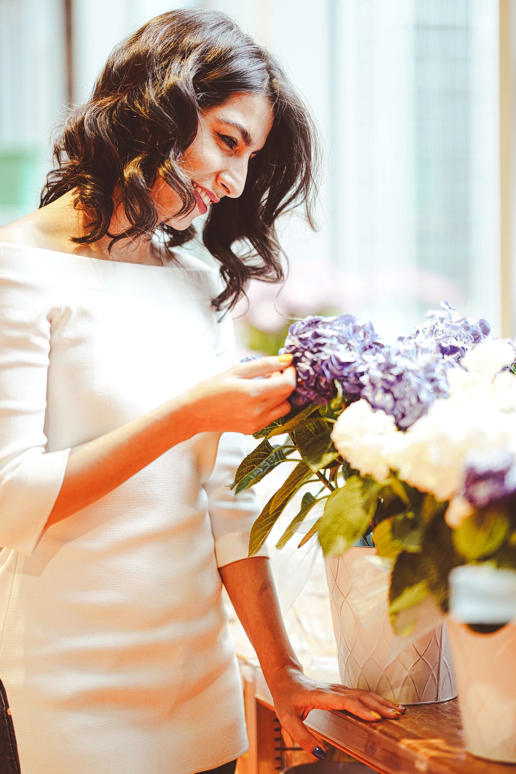Woman admiring purple and white flowers in a bright room.
