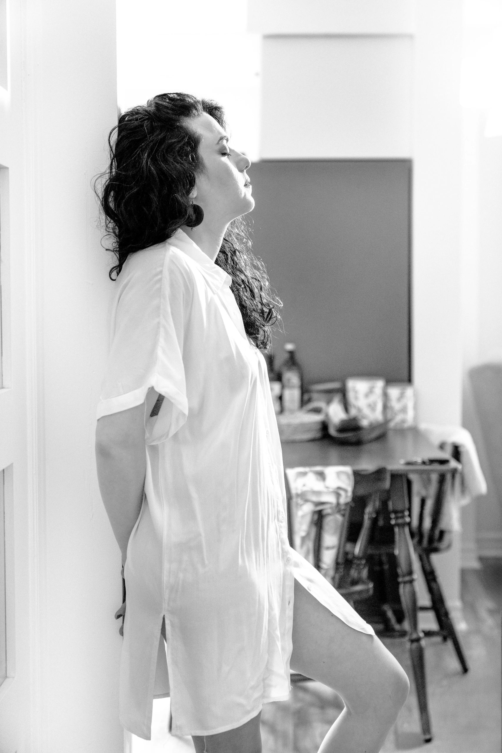 Woman with closed eyes leaning against a wall in a relaxed pose.