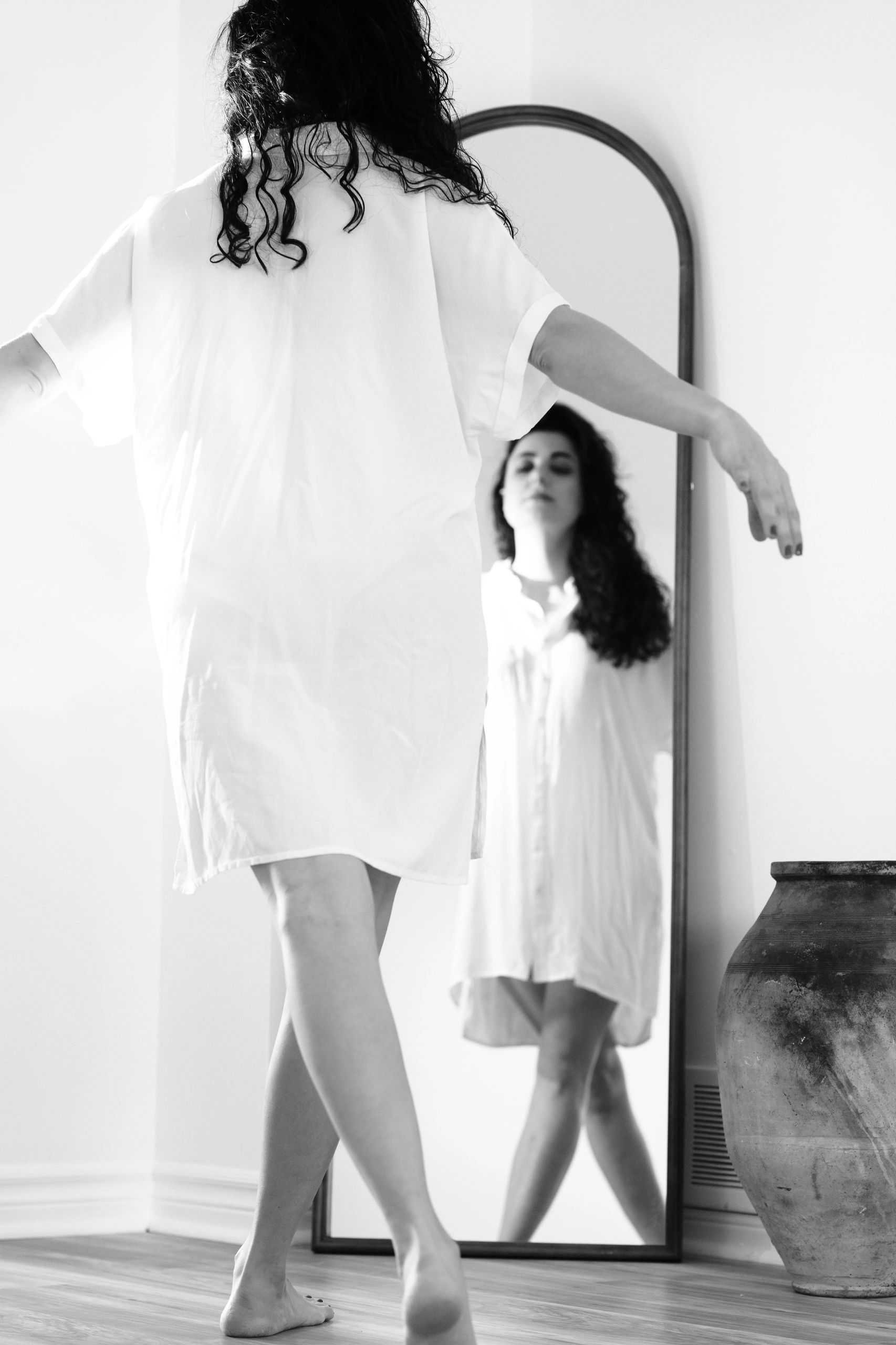 Woman in white dress dancing barefoot in front of a mirror. High-end portrait photographer in Toront