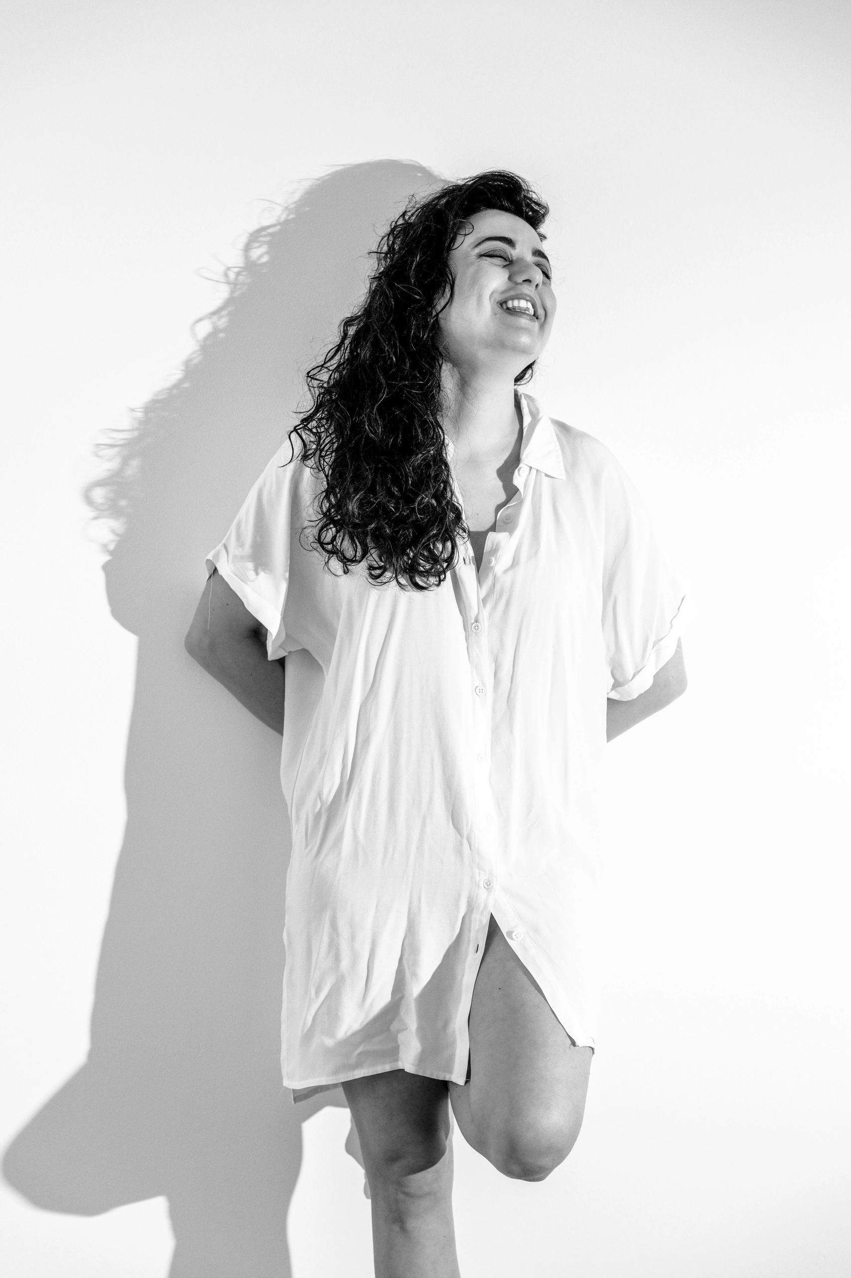 Smiling woman with curly hair in a white shirt against a white background. Stylish solo portrait ses