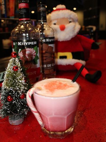 Festive holiday drink with candy cane and Santa decoration on red table.