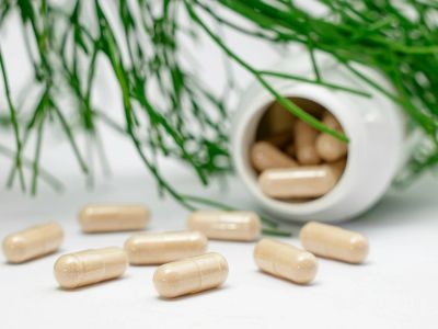 Beige capsules scattered near a white bottle with green plant background.