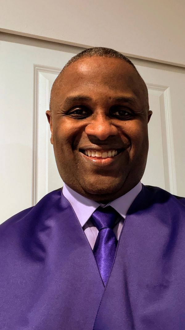 Smiling man in purple graduation attire.