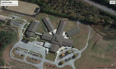 Aerial view of a large building complex with surrounding parking lots and adjacent greenery.