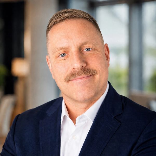 Confident man in a suit with a mustache smiling gently.