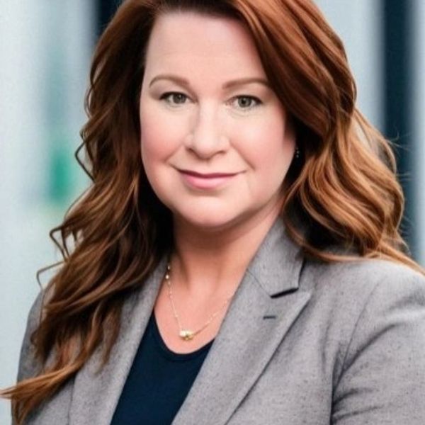 Professional woman with long red hair wearing a gray blazer and a subtle smile.