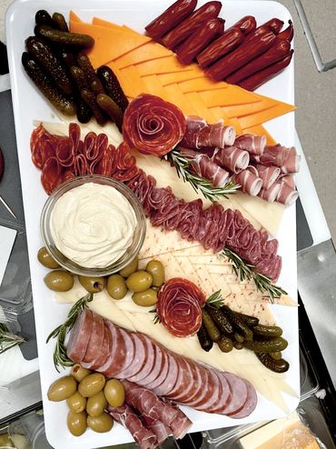 A gourmet charcuterie board with meats, cheeses, olives, pickles, and a creamy dip.