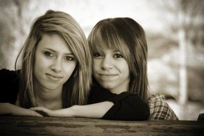 Two young women posing closely together, smiling gently.