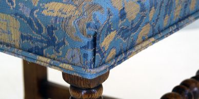 Corner of chair or bench reupholstered in  blue fabric showing double welting and knife edge tuck.