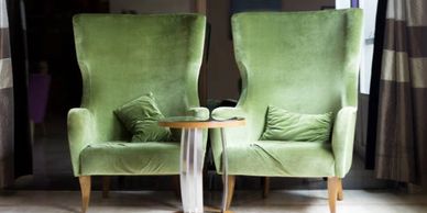 Two chairs and two pillows upholstered in shimmering green fabric.