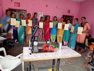 A group of women holding certificates in a room with a sewing machine.